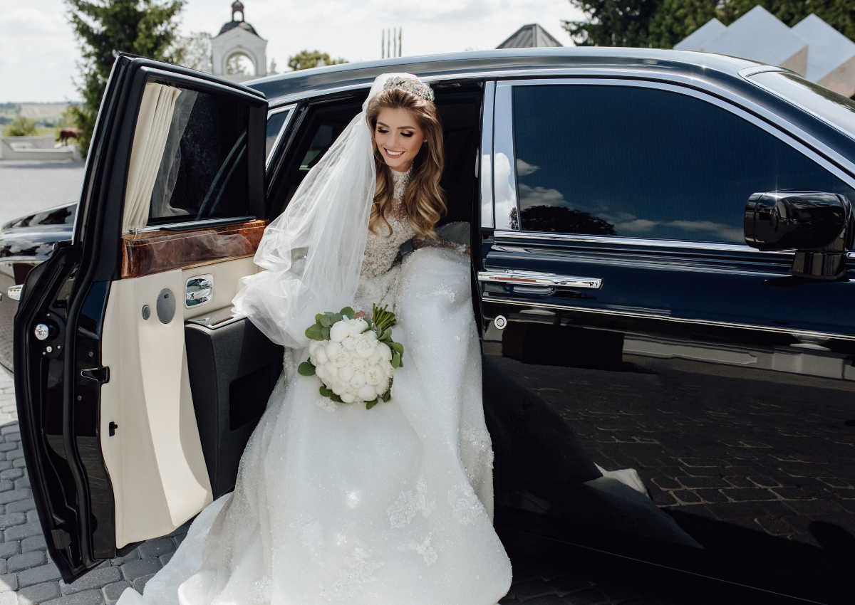 Bride exiting a luxury limousine, holding a bouquet of white flowers, in a wedding setting, emphasizing premium wedding transportation services in Sandy Springs, GA.